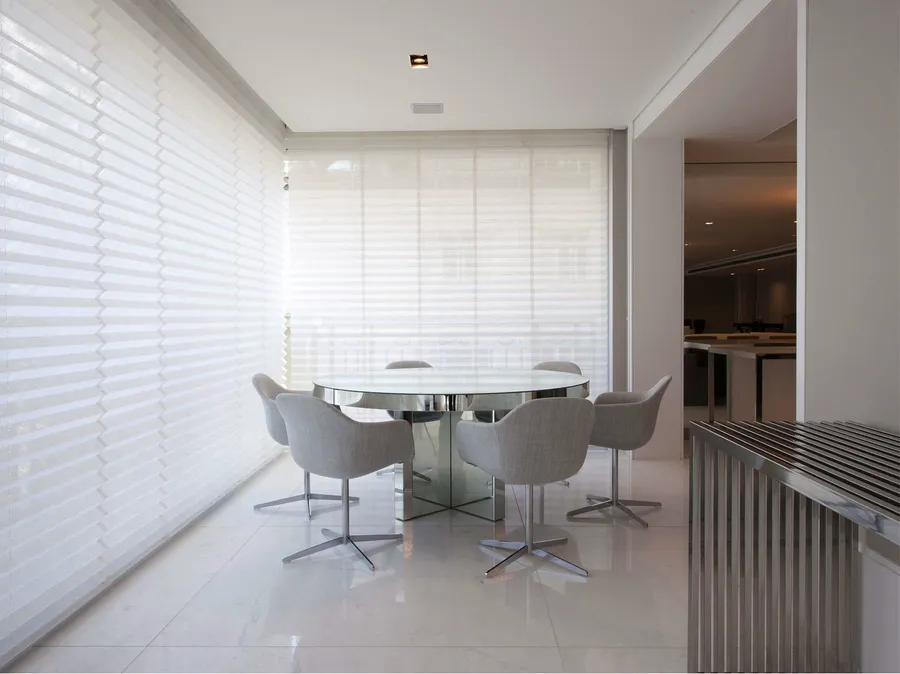 Sala de jantar clara com persianas translúcidas cobrindo a parede de janelas.