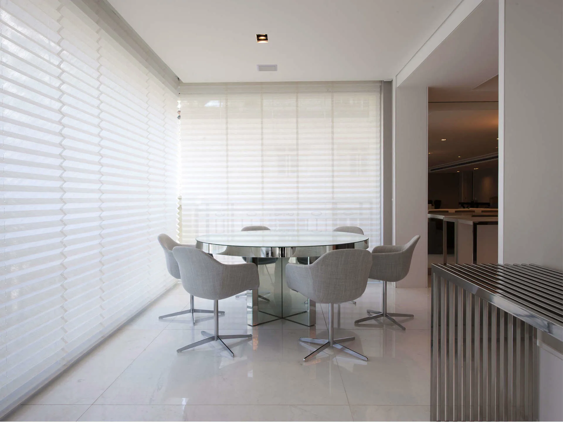 Sala de jantar clara com persianas plissadas brancas cobrindo duas paredes de janelas.