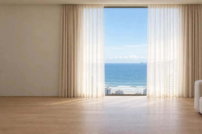 A mesma janela para o mar com cortinas de tecido leve abertas nas laterais.