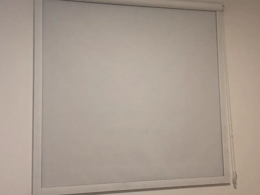 Rolo blackout branco com guias laterais e caixa superior, instalado por fora do vão numa parede clara.