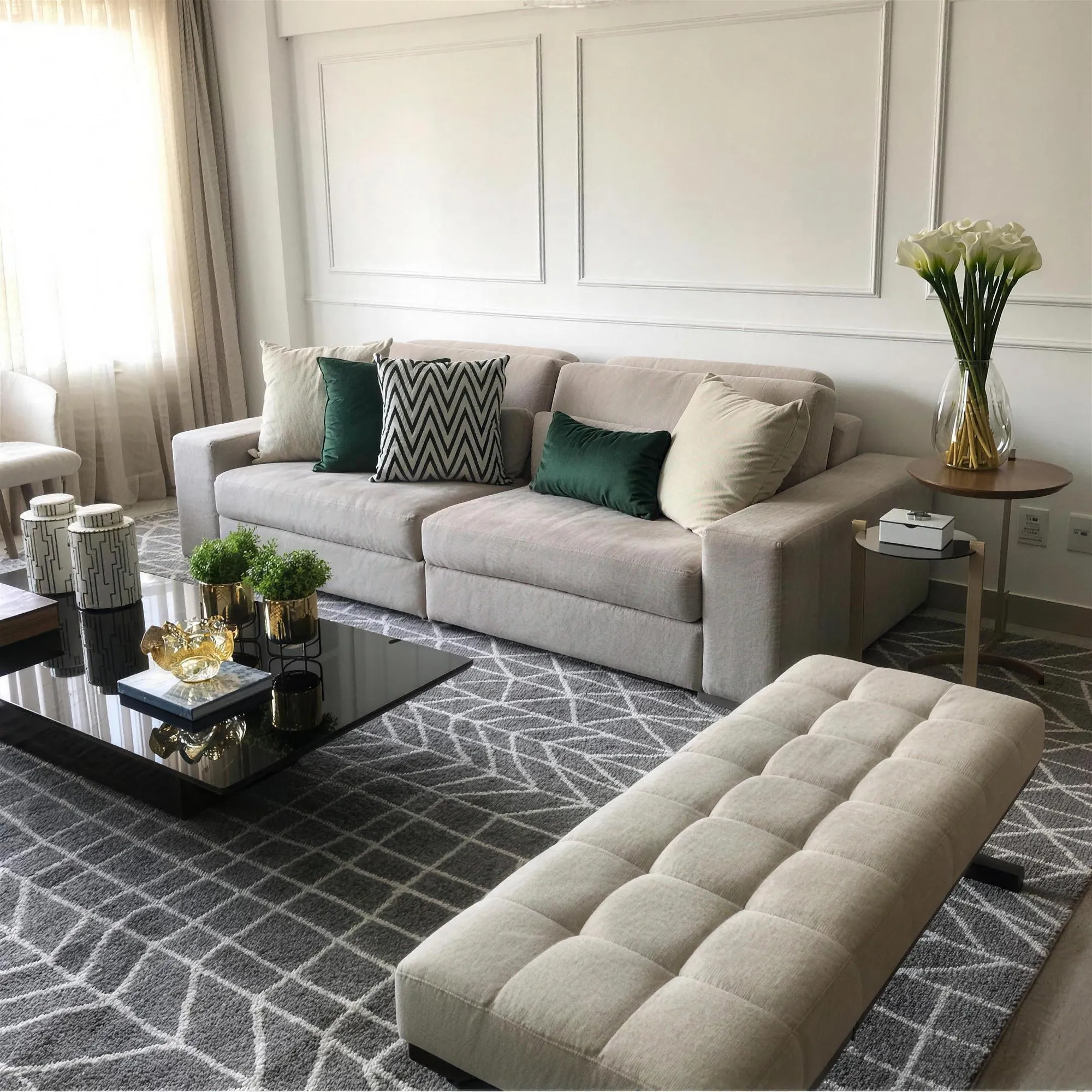 Sala clara com molduras de boiserie brancas na parede atrás de um sofá cinza-claro com almofadas verdes.