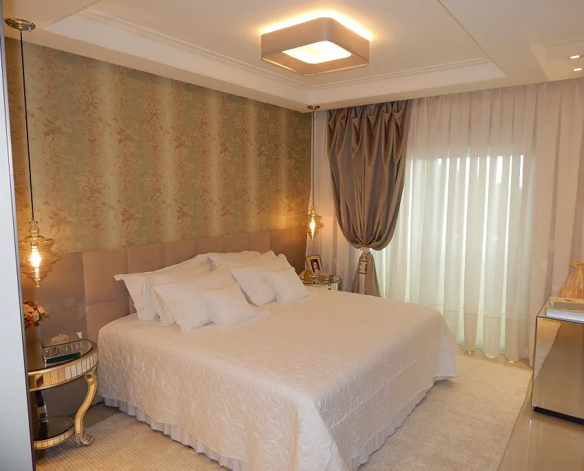 Quarto com cortina branca translúcida e cortina cinza-amarronzada presa por abraçadeira ao lado da cama.