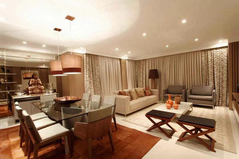 Sala de estar e jantar integradas, com cortinas bege do teto ao piso e luz quente.