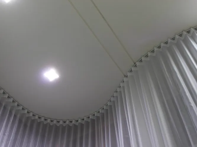 Trilho curvo no teto com cortina branca translúcida em ondas regulares.