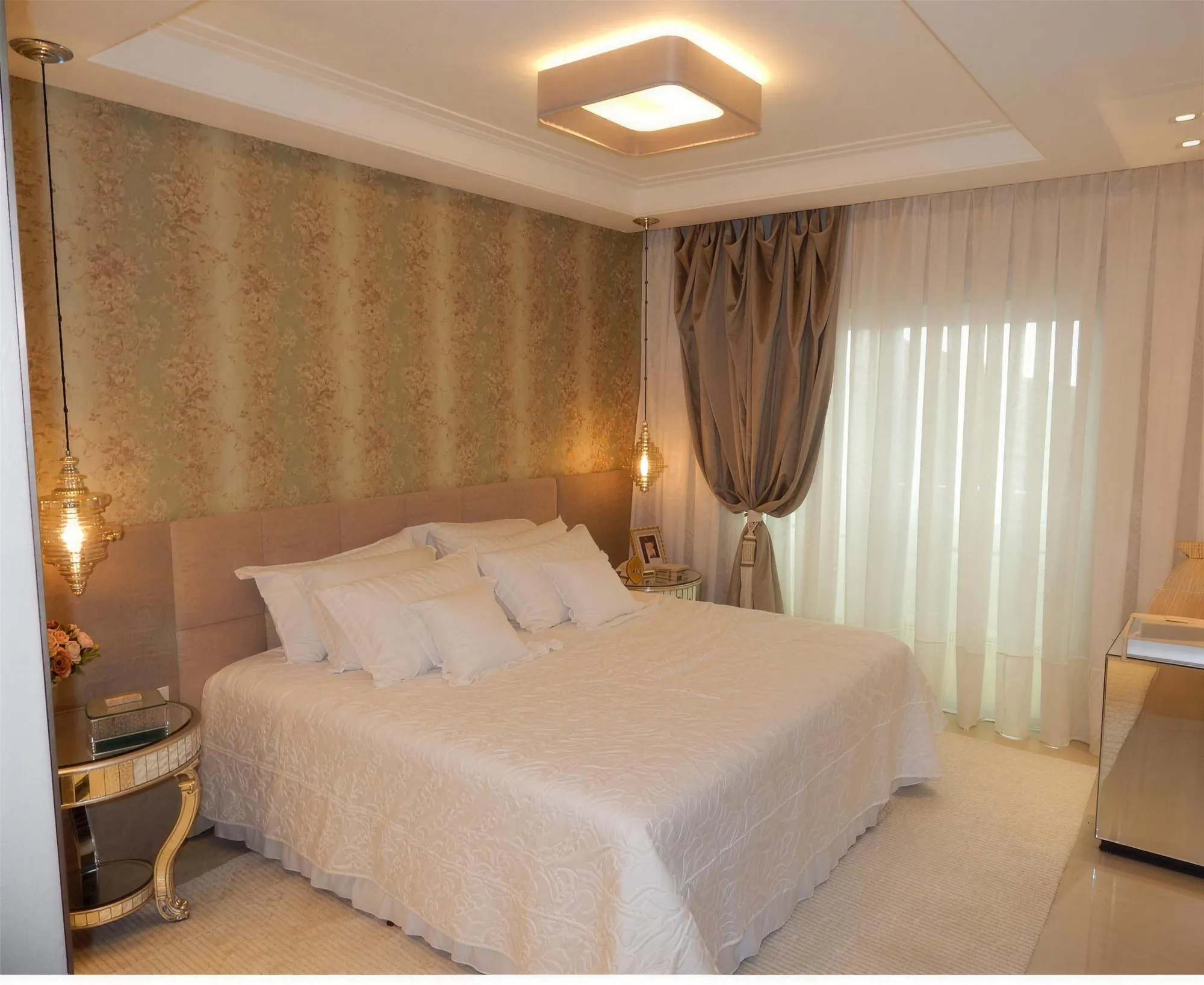 Quarto com cortina branca translúcida e cortina cinza-amarronzada presa por abraçadeira ao lado da cama.