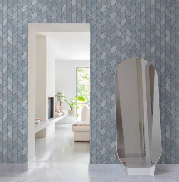Parede com papel de parede de pétalas em azul-acinzentado, passagem para uma sala clara e espelho apoiado no chão.