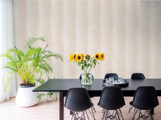 Sala de jantar clara com papel de parede bege de textura listrada, mesa preta, cadeiras pretas e girassóis.