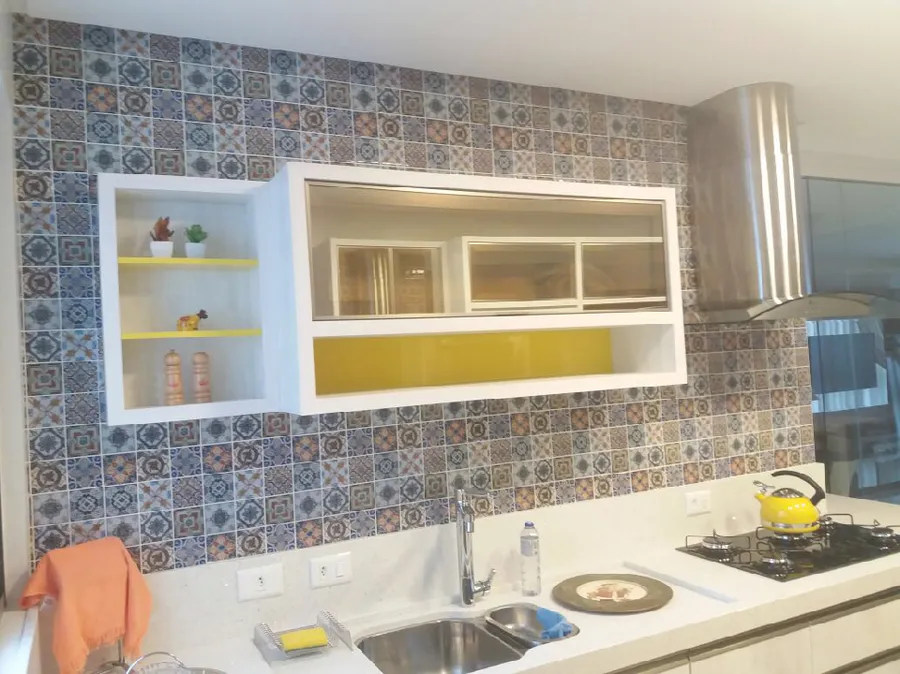 Cozinha com pastilhas estampadas em azul, laranja e bege atrás da pia e de nichos brancos com fundo amarelo.
