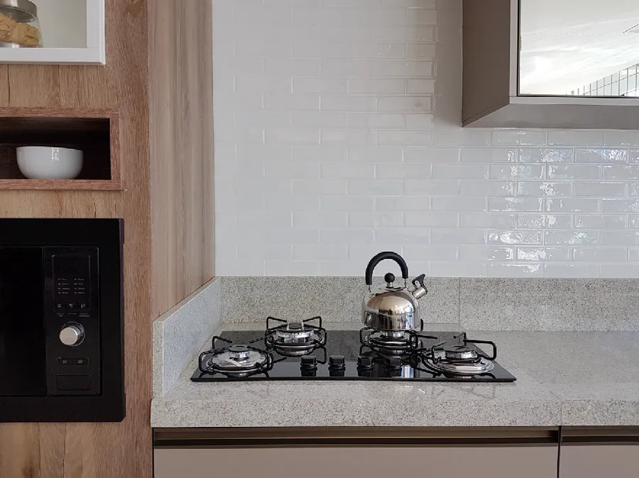 Cozinha com pastilhas brancas retangulares e brilhantes atrás do cooktop.