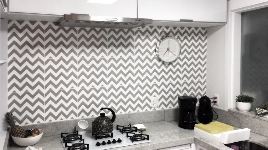 Parede de cozinha com pastilhas em zigue-zague cinza e branco, relógio e cooktop.