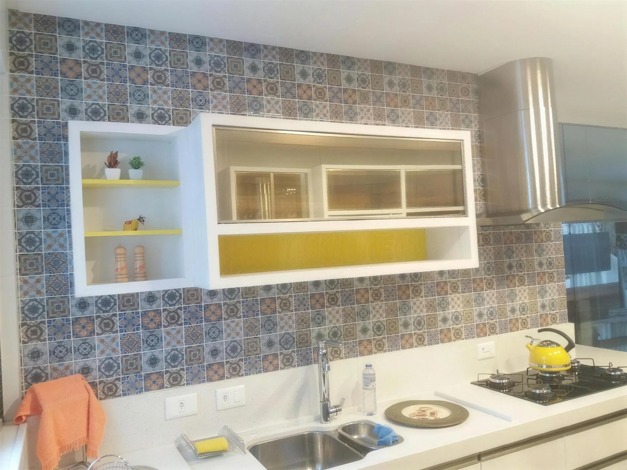 Cozinha com pastilhas estampadas em azul, laranja e bege atrás da pia e de nichos brancos com fundo amarelo.