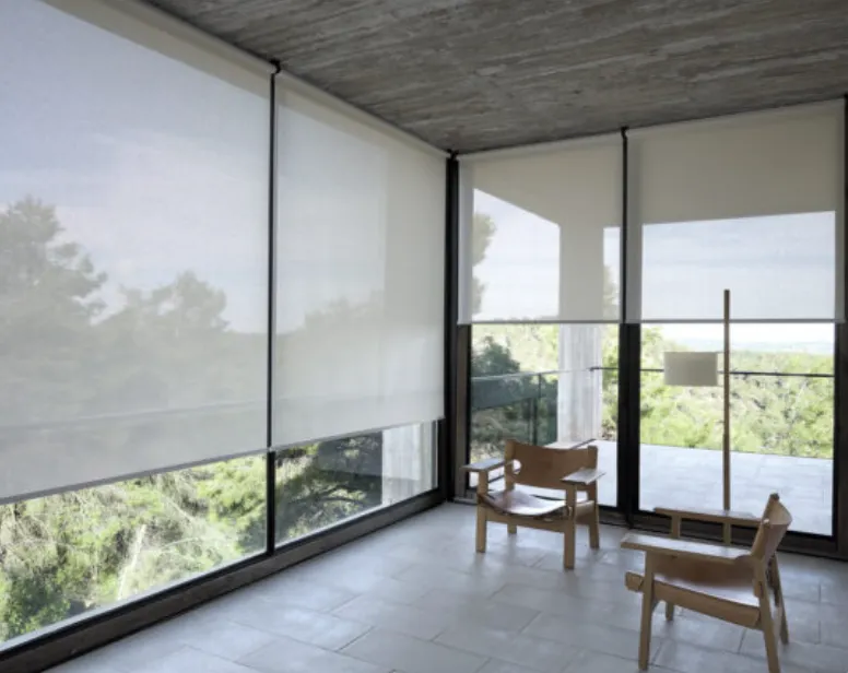 Varanda envidraçada com persianas rolo em tela solar, poltronas de madeira e vista para as árvores.