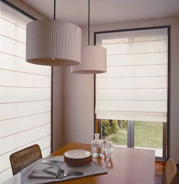 Sala de jantar com cortinas romanas translúcidas e duas luminárias pendentes sobre a mesa.
