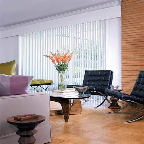 Sala com persianas verticais brancas, poltronas de couro preto e piso de madeira.