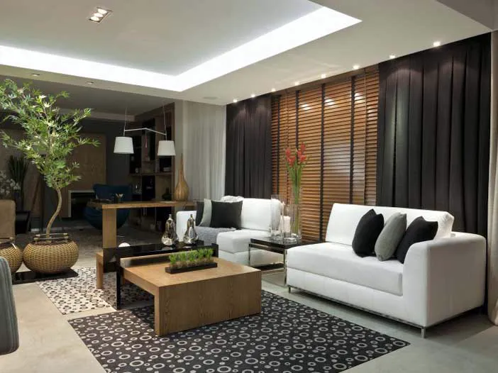 Sala de estar com persiana de madeira entre cortinas escuras, atrás de sofás brancos.