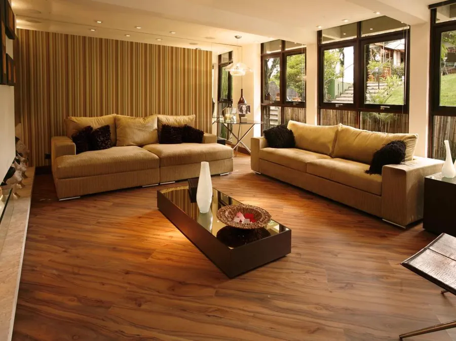 Sala de estar com sofás bege, janelas para o jardim e piso laminado amadeirado escuro.