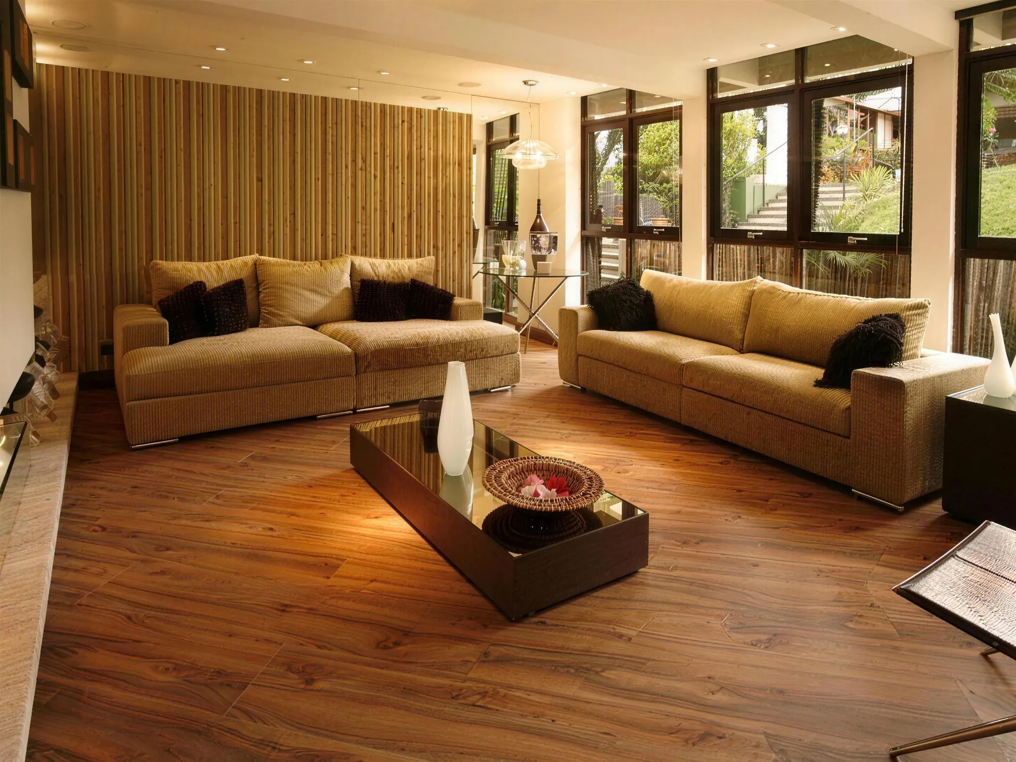 Sala de estar com sofás bege, janelas para o jardim e piso laminado amadeirado escuro.