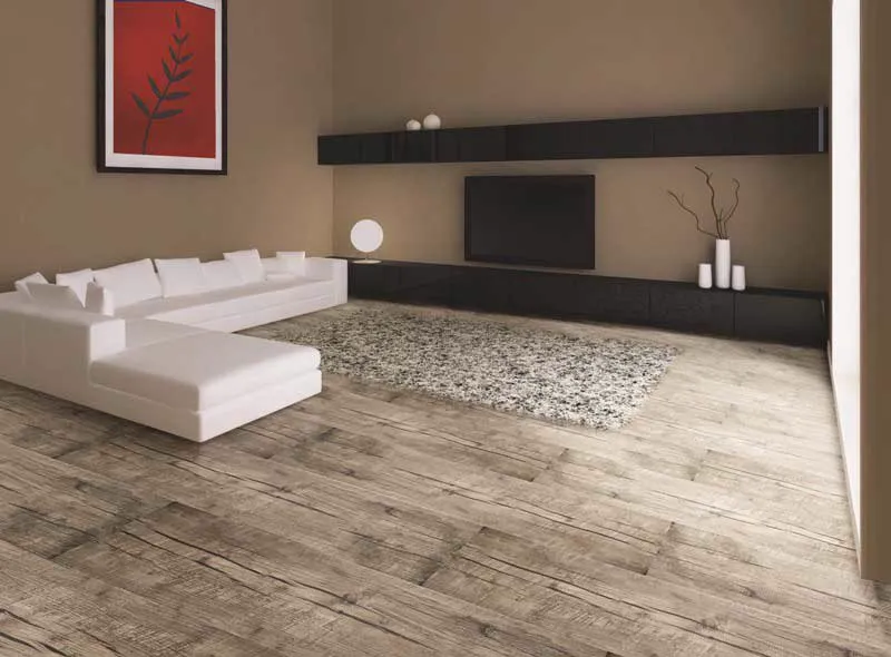 Sala com sofá branco em L, tapete felpudo e piso vinílico rústico acinzentado.