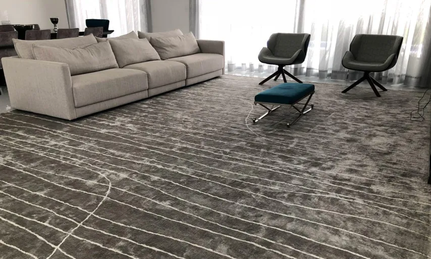 Sala clara com sofá cinza, poltronas escuras e tapete grafite com linhas brancas sinuosas.