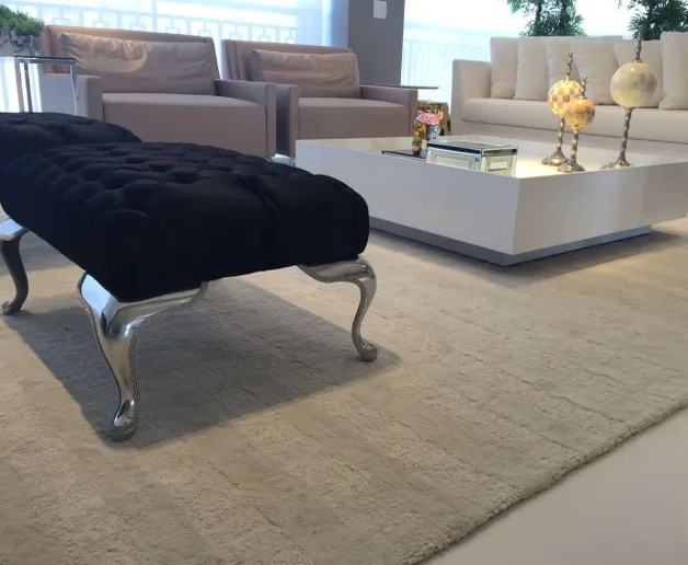 Sala com puff capitonê preto, mesa de centro branca e tapete claro de textura sutil.