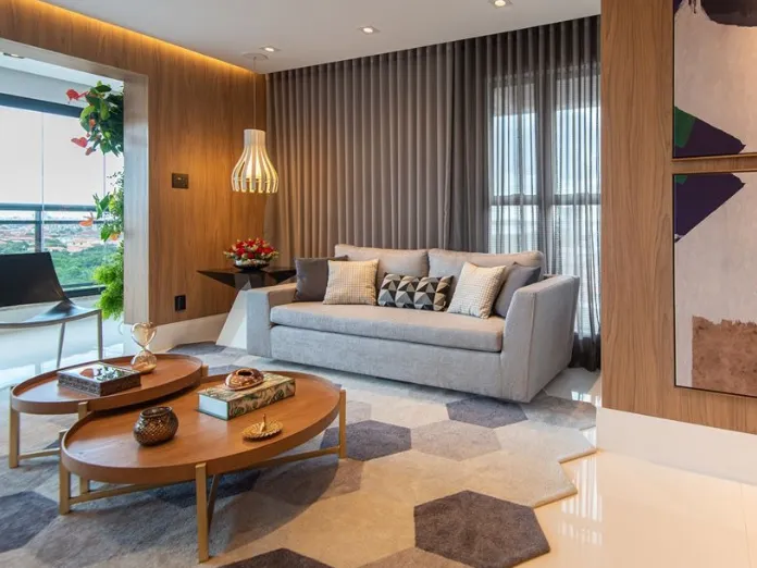 Sala com painel de madeira, sofá cinza e tapete recortado em hexágonos de tons cinza e areia.