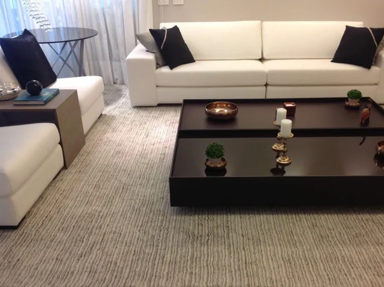Sala com sofás brancos, mesa de centro escura e tapete claro de textura listrada.