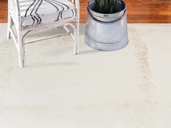 Cadeira de vime branca e vaso de planta sobre tapete felpudo em tom creme.