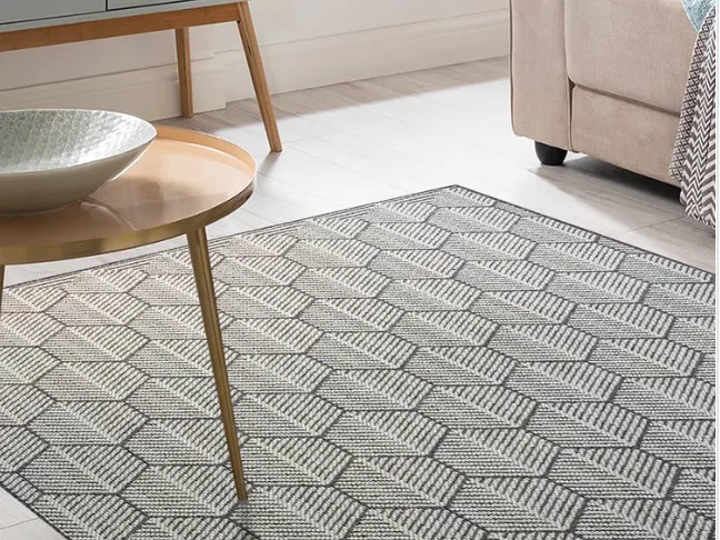 Mesa lateral dourada e poltrona bege sobre tapete de trama plana com desenho de hexágonos em cinza.