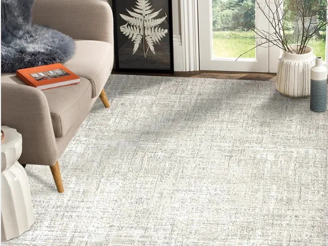 Canto de sala com poltrona bege, quadro de folhagem e tapete claro de textura mesclada em cinza.