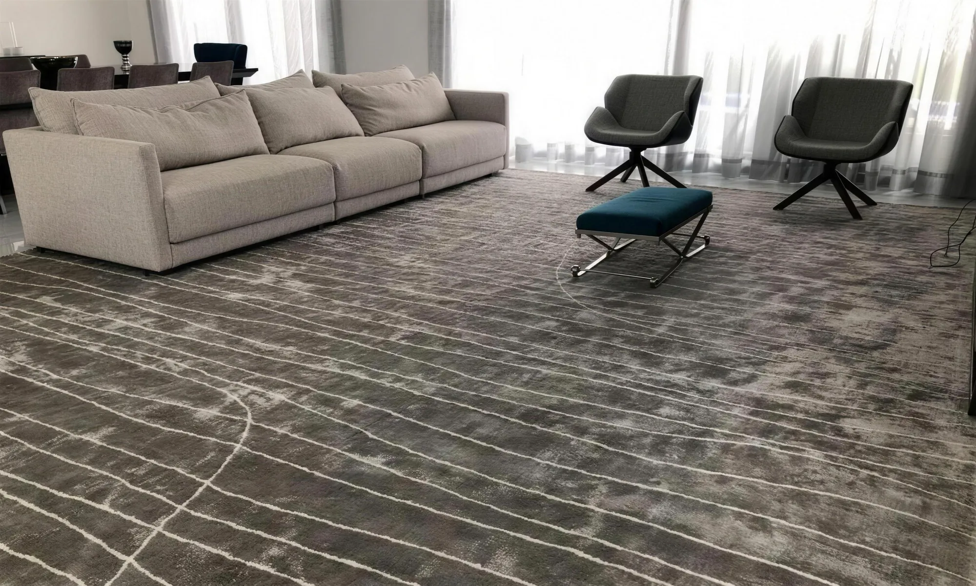 Sala clara com sofá cinza, poltronas escuras e tapete grafite com linhas brancas sinuosas.